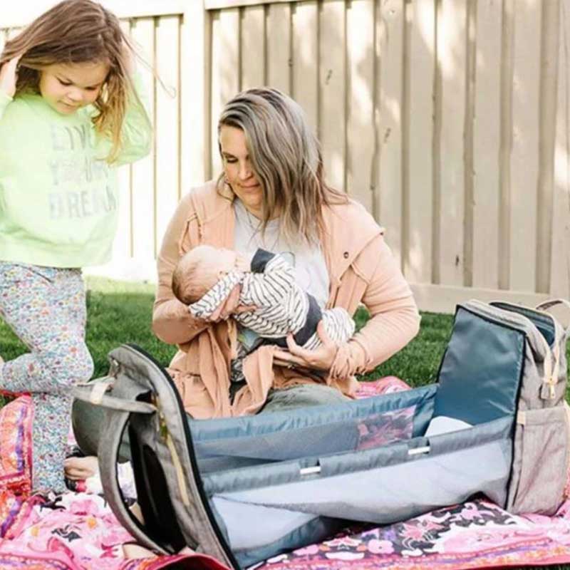 Une maman couche son bébé dans son sac a langer transformable en lit couffin